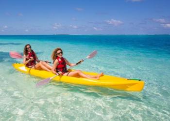 Donna in bikini su paddleboard giallo in acque cristalline.