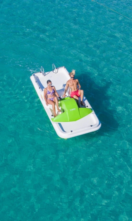 Due persone su un pedalò verde in mare, una nuota vicino alla corda.