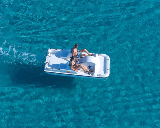 Mare cristallino con pedalò e scogli, persone che nuotano.